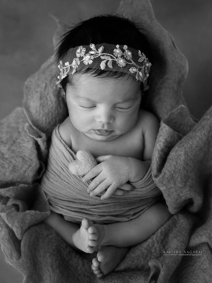A black and white version of a newborn girl in a basket. The monochrome tones highlight the textures of the wrap and her peaceful, sleeping face.