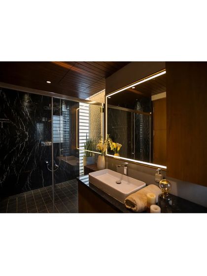 The master bathroom features a dark and moody palette, with black marble walls and a wood-paneled ceiling. The clean lines of the vanity and the backlit mirror create a sophisticated and spa-like atmosphere.