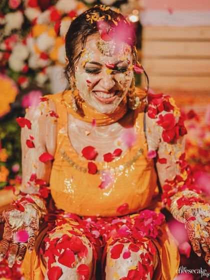 A candid shot of the bride during her 'phoolon ki haldi', her smile shining through the turmeric and rose petals.