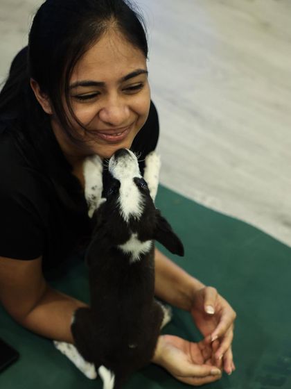 A participant lies on her stomach, smiling as a black and white puppy looks up at her, ready to play.