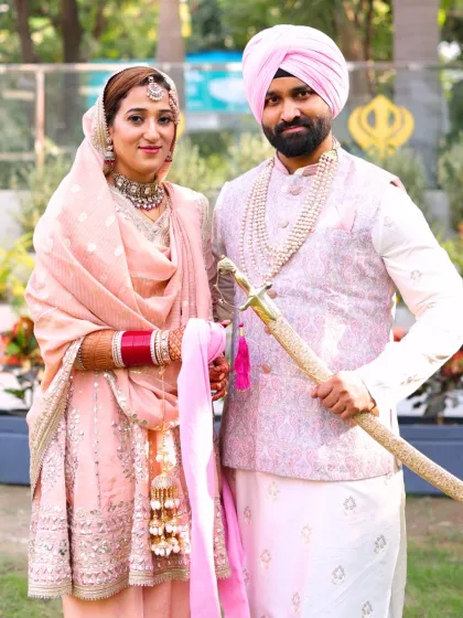 The couple poses with the traditional kirpan. The bride's makeup is flawless, with a focus on radiant skin that glows against her pastel pink attire.