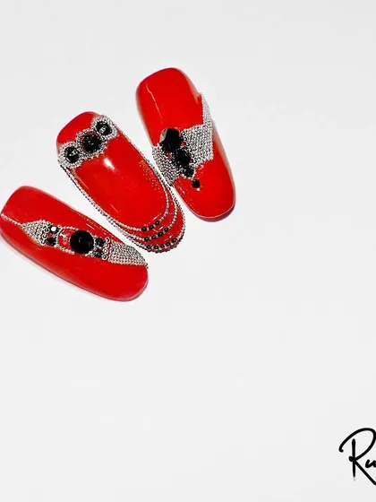 A bold red nail set with intricate black and silver crystal jewellery.
