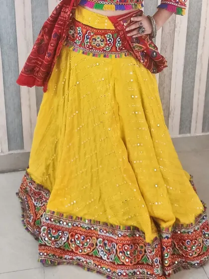 A side view focusing on the skirt of the yellow chaniya choli. This shot highlights the mirror work scattered across the skirt and the dense, vibrant embroidery along the hem.