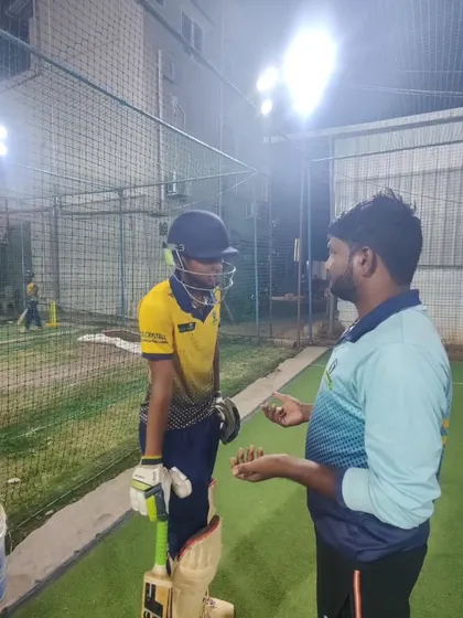A coach giving tactical advice to a young batsman during a night session. We focus on both the technical and mental aspects of the game.