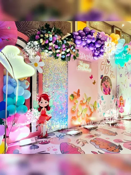 A colorful and whimsical photo opportunity at a fairy and butterfly themed party. The setup includes a custom floor decal, a sequin backdrop, and a mix of floral and balloon arrangements.