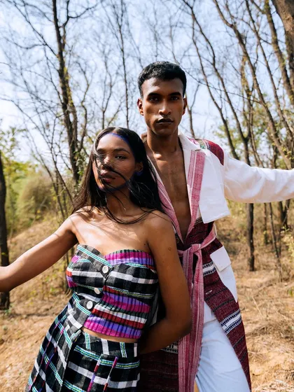 A dynamic dual-model shot from the "Nazaar" outdoor editorial. The models' poses are strong and expressive, interacting with the natural, wooded environment.