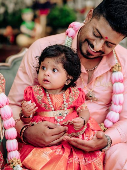 A precious moment with a father and his baby girl. Her tiny red and gold pattu pavadai was designed to be a miniature version of traditional elegance.