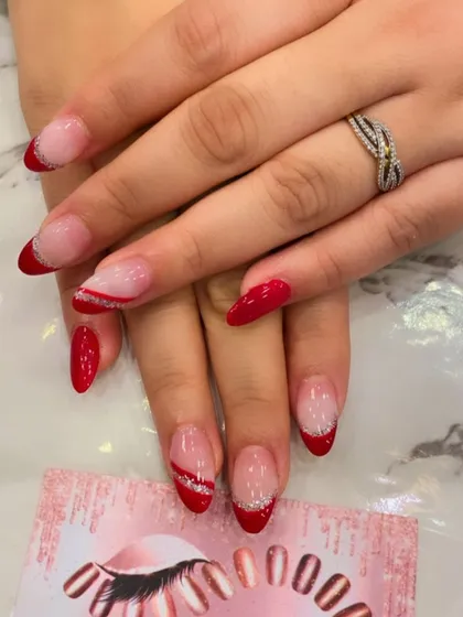 A creative twist on the French manicure. This set features red tips on almond-shaped nails, with one accent nail showing an abstract red and silver glitter design.