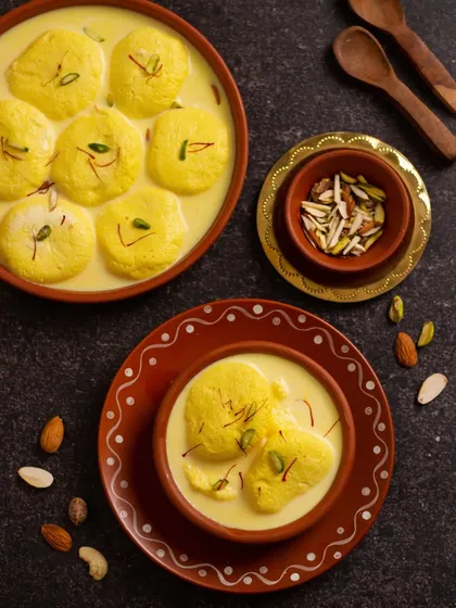 A beautiful flatlay of Ras Malai, a creamy milk-based dessert. The dark background makes the yellow of the saffron-infused milk pop.