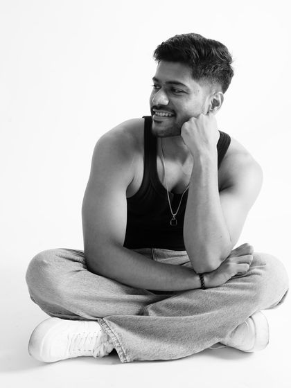 A smiling, cross-legged pose in black and white. This image shows a different side of a fitness model, combining a powerful physique with a warm and engaging personality.