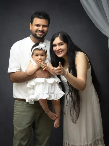 A fun and interactive family portrait. The mother pointing towards the camera adds a playful element to this classic studio setup.