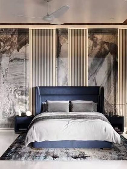 A contemporary bedroom with a bold accent wall featuring marble-patterned panels and vertical backlighting. The deep blue upholstered bed adds a touch of color and luxury to the modern design.
