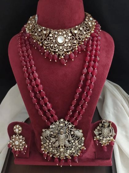 This grand bridal set in a rich maroon color features a Victorian choker and a matching long necklace with a large pendant. The design incorporates traditional motifs like elephants and deities.