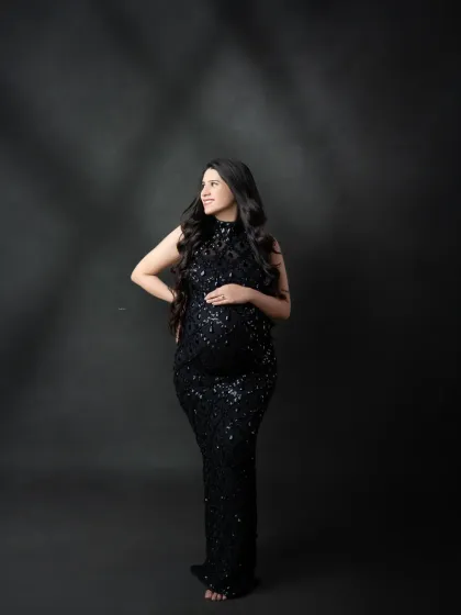 A classic studio portrait with dramatic lighting. The mother-to-be looks radiant in her black sequin gown, a timeless choice for an elegant maternity shoot.