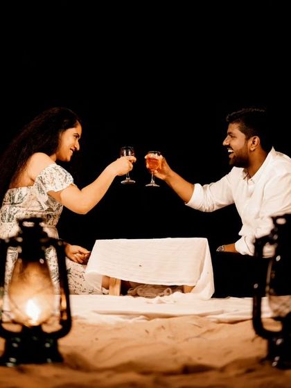 A couple enjoys a romantic picnic on the beach at night, toasting each other under a string of lights. This shot captures the magical ambiance of a styled setup.