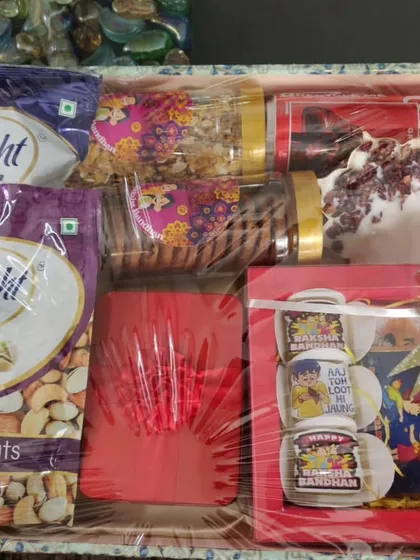 The contents of the Rakhi tray, including mixed nuts, a sipper, and a personalized chocolate frame.