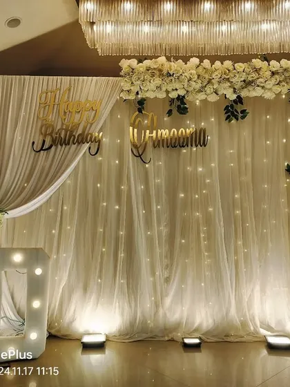 For an 80th birthday, we designed this elegant floral arrangement. It features a beautiful arch of white artificial flowers over a draped backdrop with fairy lights, complemented by a large "80" marquee number, proving that our decor services extend beyond just balloons.
