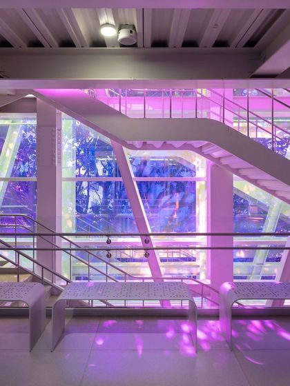 The dynamic play of colored light on the main staircase at the MAP museum. The use of dichroic film on the glass facade transforms the circulation space into an immersive art experience, changing with the time of day and the movement of people.