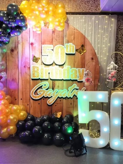 A rustic-themed 50th birthday party decoration. We used a wooden panel backdrop, a colorful balloon arch, and light-up '50' marquee numbers to create this look.