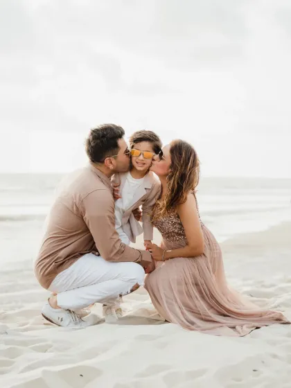 A sweet family photo with both parents kissing their son's cheeks on the beach. A beautiful way to celebrate a milestone birthday.