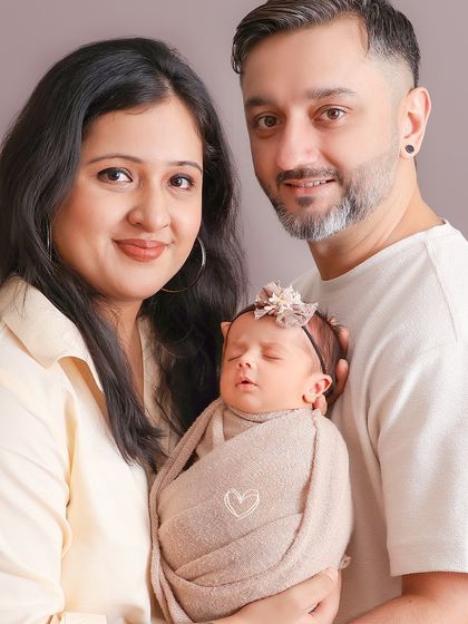 A beautiful family of three looking towards the camera. This shot captures both the parents' pride and the serene beauty of their sleeping newborn.