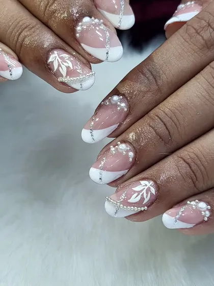 An example of our delicate bridal nail artistry. This elegant design combines a classic white French tip with hand-painted white leaves and carefully placed pearl chains for a romantic and timeless wedding day look.