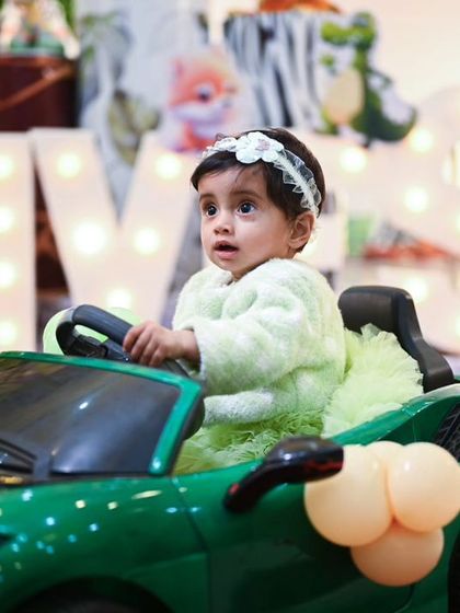 Ready to drive into her first birthday party! The birthday girl sits in a miniature green sports car, part of an elaborate jungle-themed decoration setup.