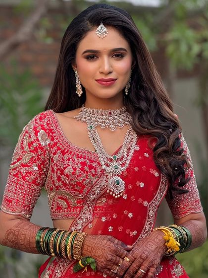 A full portrait of the bride in her red lehenga. The makeup is bold and beautiful, perfect for making a statement at her wedding reception.