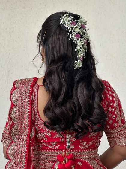 A view of the intricate bridal hairstyle, adorned with delicate baby's breath. The soft waves and floral details add a touch of romance to the traditional red lehenga look.