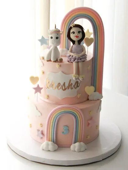 A magical unicorn and rainbow cake for Kresha's 3rd birthday. This two-tiered pastel pink cake is adorned with a custom girl-and-unicorn topper and sweet rainbow details.