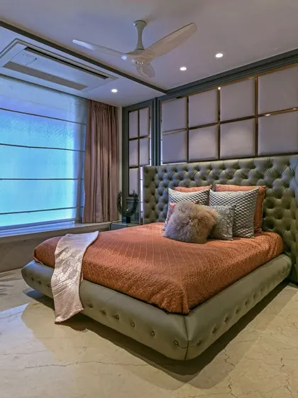 A wider shot of the same bedroom, showing the large window and indoor plant that bring natural light and life into the space. The design feels both luxurious and livable.