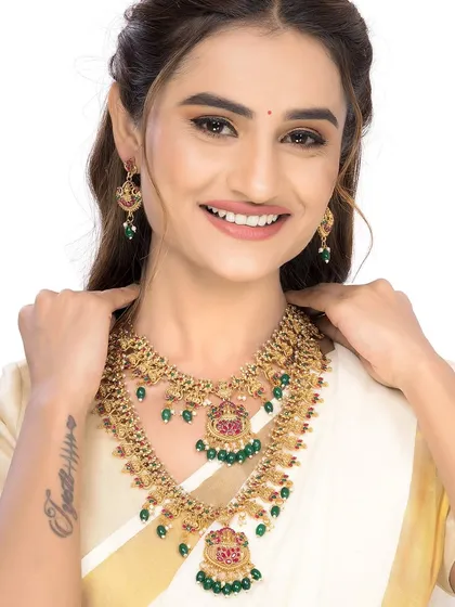 This cheerful shot captures a model wearing a traditional South Indian necklace set with green and pink stones. Her smile and the clean white background make the image feel fresh and perfect for e-commerce listings.