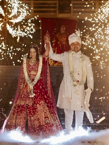 A spectacular Varmala moment in Jaipur, with the couple framed by cold pyro fireworks against a backdrop of traditional red decor.