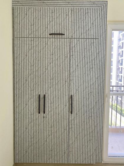 A three-shutter wardrobe with a unique vertically-grooved, marble-textured laminate and minimalist black handles.