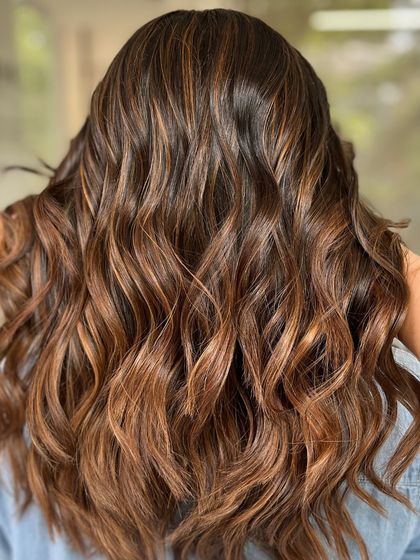 Golden tones that warm the soul. This balayage features beautiful, warm highlights styled into bouncy curls.