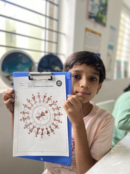 A young boy displays his intricate Warli art piece, which focuses on symmetry and composition. Our classes often explore different cultural art forms to broaden our students' creative horizons.
