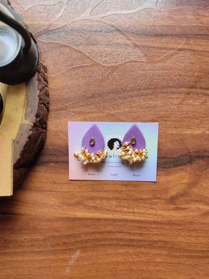 These purple fabric earrings are decorated with a cluster of pearl and gold beads. They are a beautiful choice for pairing with a traditional silk saree.