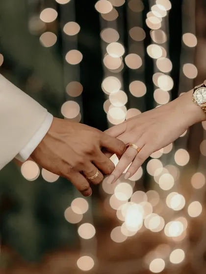 A close-up of the couple holding hands, showcasing their new engagement rings against a beautiful bokeh background.