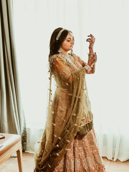 A full-length shot of the bride, Maitri, as she gets ready. The natural light from the window beautifully illuminates her pastel lehenga.