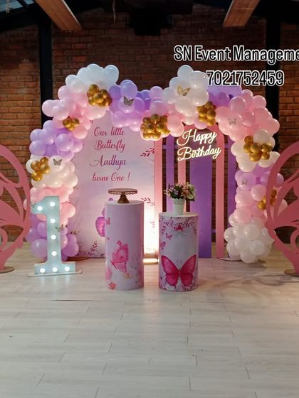 A sweet butterfly theme for "Our Little Butterfly" turning one. This setup features large pink butterfly wing props, a custom backdrop, and a pink, purple, and gold balloon arch.