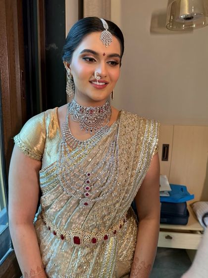 A candid moment of South Indian bride Trisha on her wedding day. She wears a stunning gold and red Manish Malhotra saree, paired with layered diamond and ruby jewellery for a regal look.