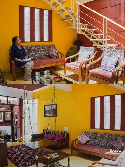 The living area of the Raghavendra Residence is a vibrant and welcoming space, with bright yellow walls, comfortable wooden furniture, and a traditional indoor swing.