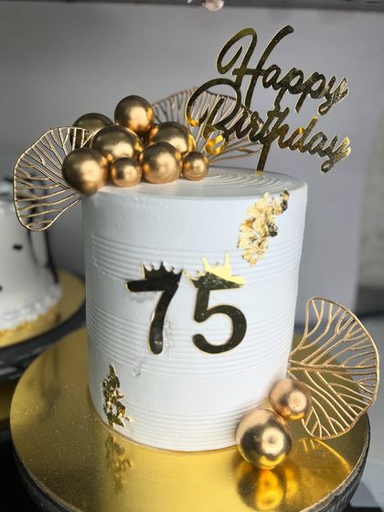 A chic and modern cake for a 75th birthday. The design is minimalist yet elegant, with golden spheres, leaf accents, and gold foil, perfect for a stylish celebration.