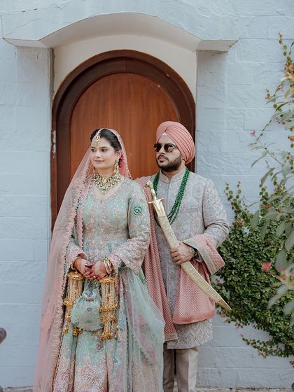 A regal portrait of a Sikh bride and groom in their stunning wedding attire. The groom holds the kirpan, a symbol of his duty to protect.