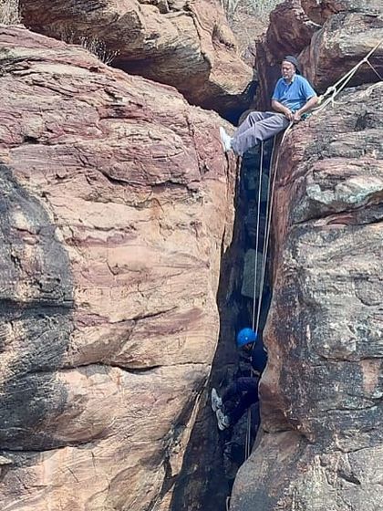 An instructor supervises a camper practicing chimney climbing, a technique used to ascend narrow gaps between rock faces in Badami.