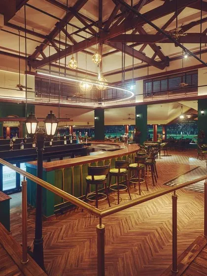 From this angle at the KGA bar, you can see how uplighting the stunning wooden ceiling trusses makes the entire space feel larger and more grand. The contrast between the illuminated ceiling and the moody, low-lit seating areas creates a dynamic and inviting ambiance.