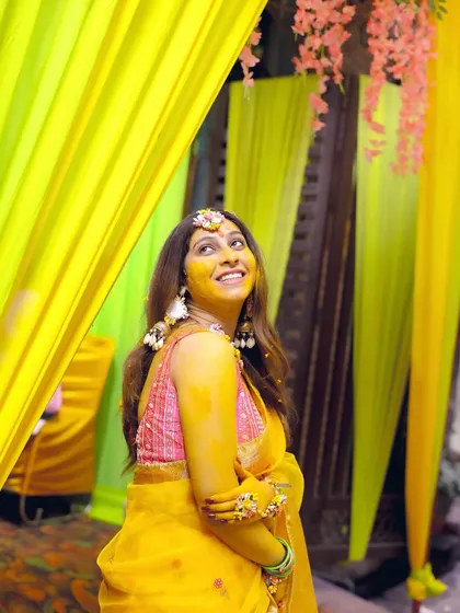 A candid shot of the bride looking up with a smile, surrounded by the bright yellow decor of her Haldi ceremony.