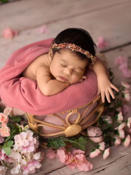 This little one is sleeping peacefully on a prop surrounded by pink flowers. The soft lighting and floral elements create a dreamy, romantic atmosphere.