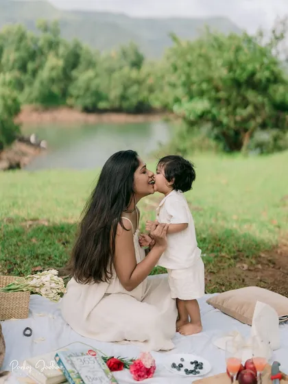 A sweet kiss between mother and son. This tender moment captures the special bond they share, set against the backdrop of their lovely lakeside picnic.