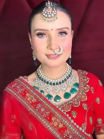 A bride in a red lehenga wearing a Kundan and green stone choker set. The simple maang tikka and nath balance the heavy necklace perfectly.